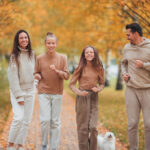 A family walking through a park in fall, there are leaves on the ground