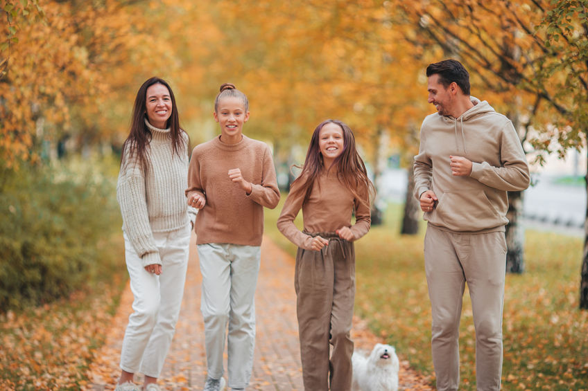 A family walking through a park in fall, there are leaves on the ground