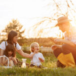 Happy young family having lunch at summer garden party. Mother, father and two kids enjoy spending time together on weekend at the countryside.