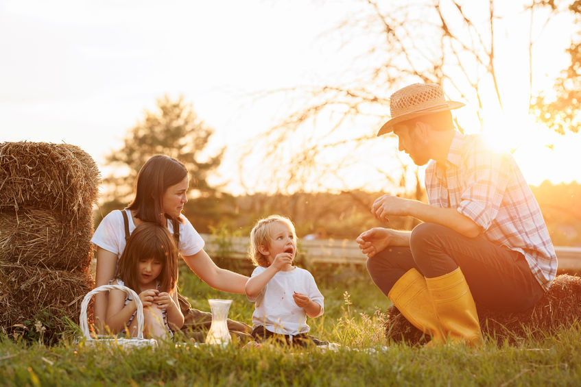 Happy young family having lunch at summer garden party. Mother, father and two kids enjoy spending time together on weekend at the countryside.